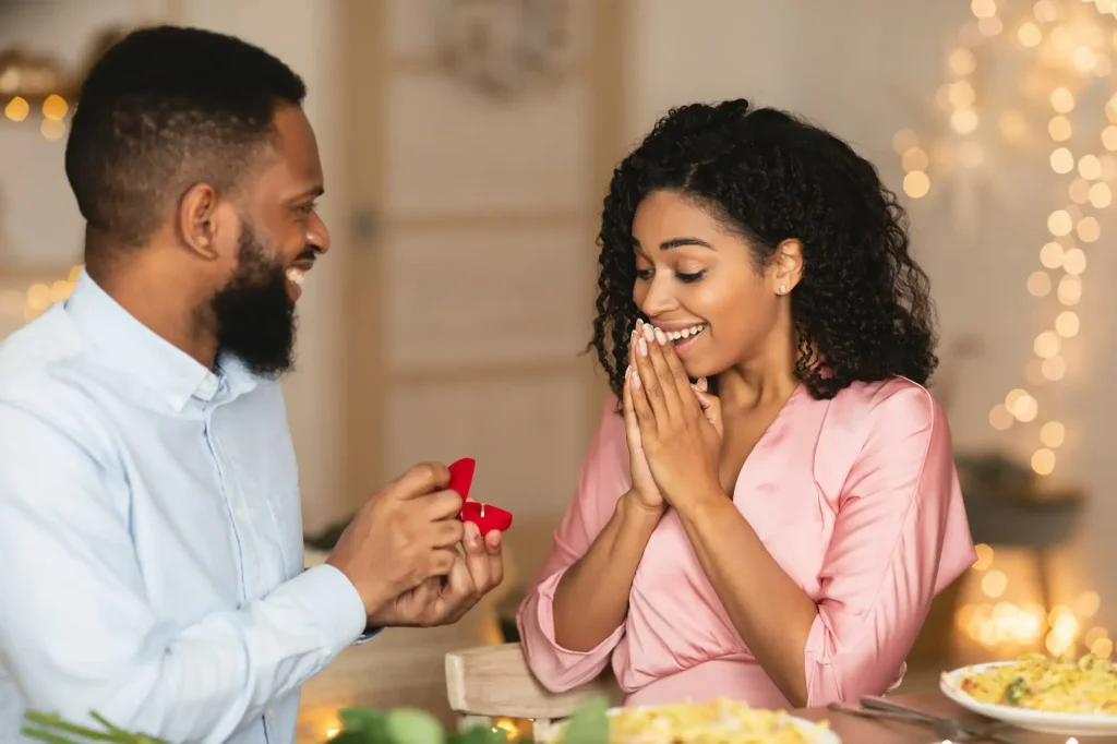 Smiling afro man making proposal with ring to his fiance