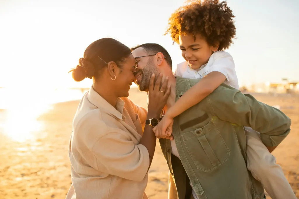 Young happy family spending time outdoors at the beach, spouses father and mother kissing, man