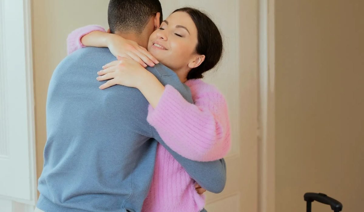 Romantic Young Couple Embracing Standing With Suitcase In Hotel Indoor