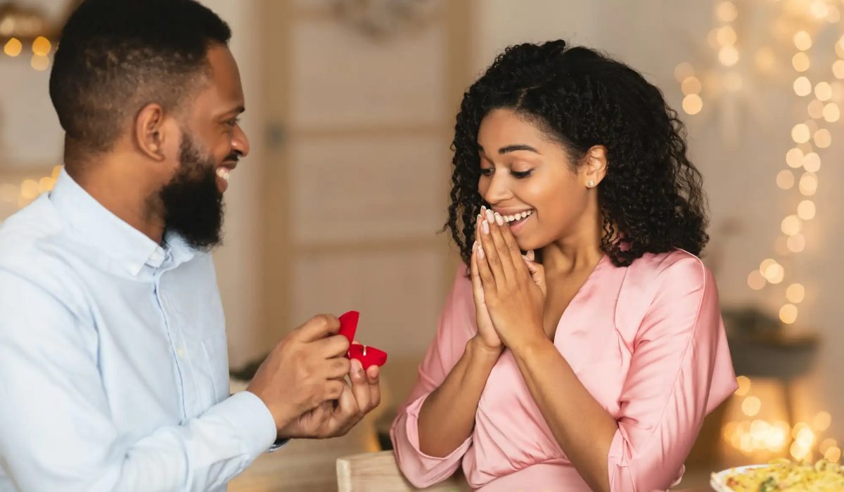 Smiling afro man making proposal with ring to his fiance
